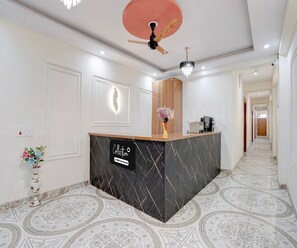 A reception area with a modern design, featuring a reception desk, a ceiling fan, and patterned flooring. - Deluxe Basai Chowk (Gurugram)