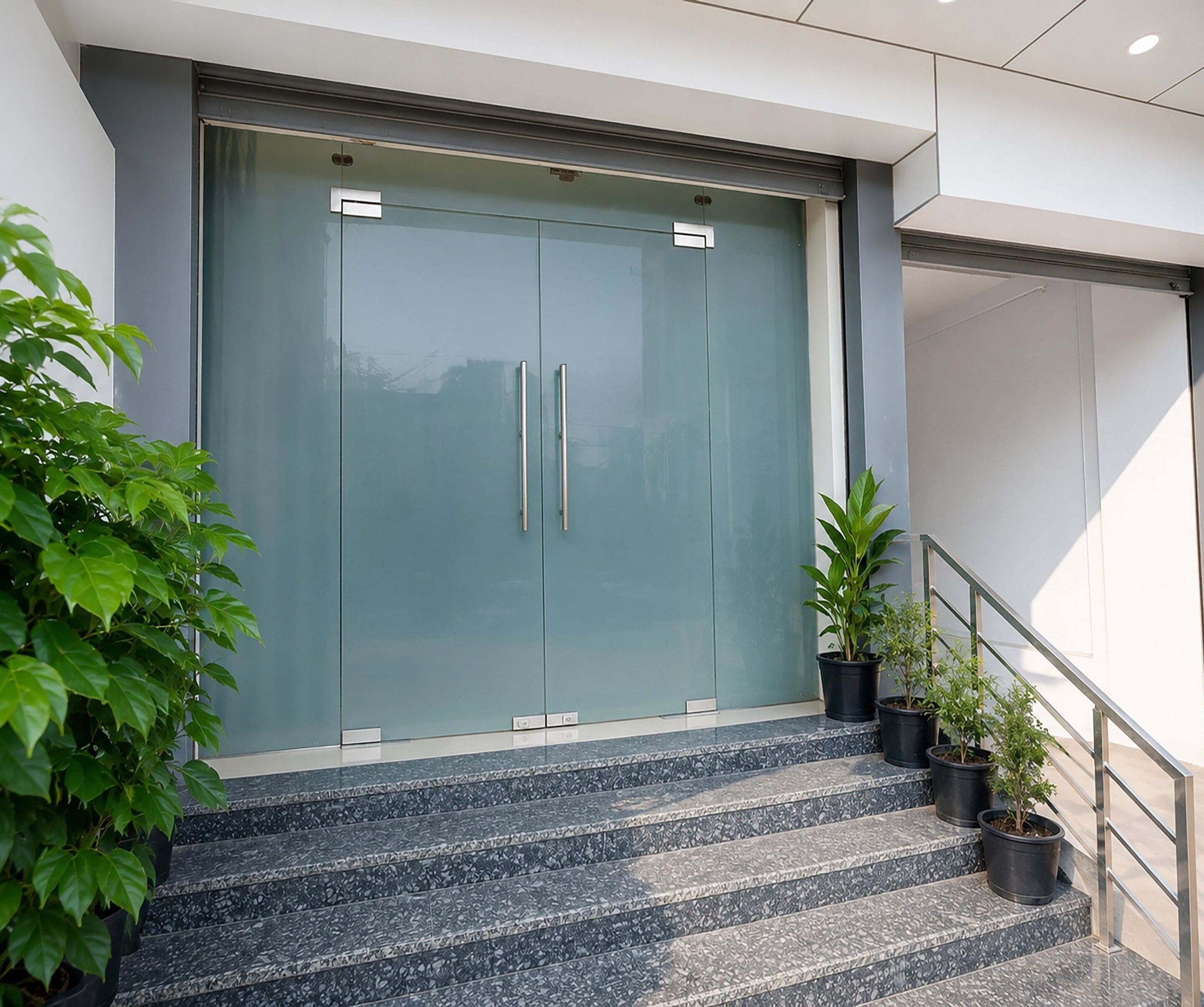 A modern building entrance with a glass door, metal handles, and a staircase leading up.
