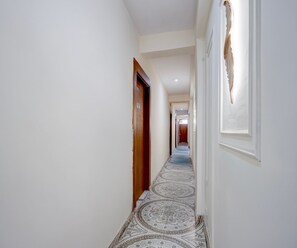 A hallway with patterned flooring, a wooden door, and a wall-mounted light fixture. - Deluxe Basai Chowk (Gurugram)