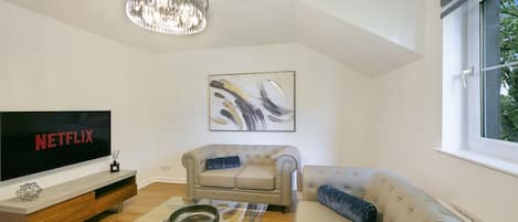 A modern living room with a flat-screen TV, a sofa, a coffee table, and a chandelier.