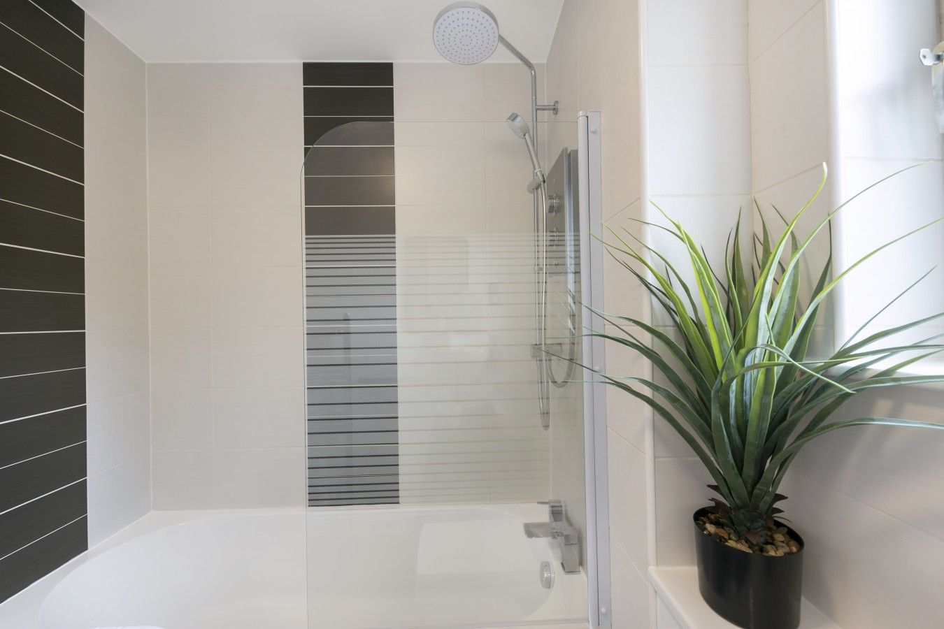 A modern bathroom with a glass shower enclosure, a white bathtub, and a potted plant.