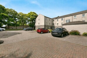 A parking area with several cars, a building with a flat roof, and a brick pathway. - Eday Lodge - Grampian Lettings (Aberdeen)