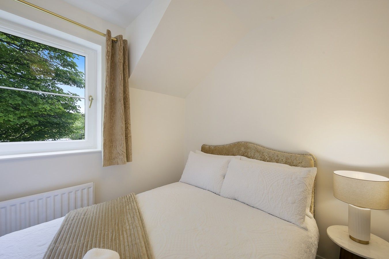 A bedroom with a bed, a window with curtains, a bedside lamp, and a radiator.