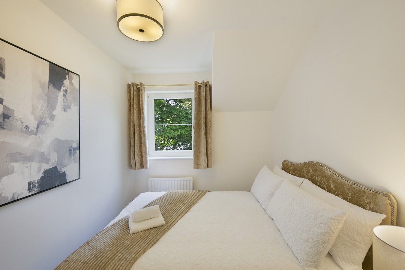 A bedroom with a bed, a window with curtains, a radiator, and a wall-mounted light fixture.