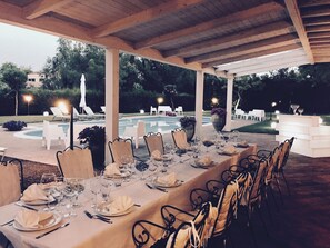 An outdoor dining area with a long table set for a meal, surrounded by chairs, and a pool in the background. - An exclusive venue for private events between Mount Etna, Taormina, and the sea! (Sicily)