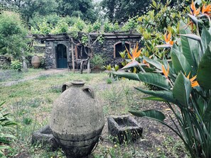 A rustic stone building with a wooden door and windows, surrounded by lush greenery and a large stone pot in the foreground. - An exclusive venue for private events between Mount Etna, Taormina, and the sea! (Sicily)