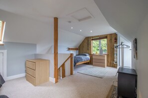 Ein Schlafzimmer mit einem Schlafplatz in der Erhöhung, einer Holzkommode, einem Schreibtisch und einer Heizung.