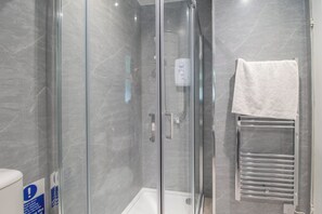 Cabina doccia in vetro con pannello comandi, un asciugamano bianco su un porta asciugamani e un cartello con istruzioni per la pulizia.