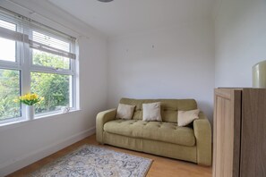 Ein Zimmer mit einer Couch, einem Fenster mit Jalousien, einer Vase mit Blumen und einem Teppich.