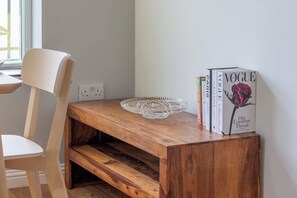 Eine Holzbank mit einer Glastafel und einem Stapel Bücher, darunter ein Vogue-Magazin, vor einer schlichten Wand.
