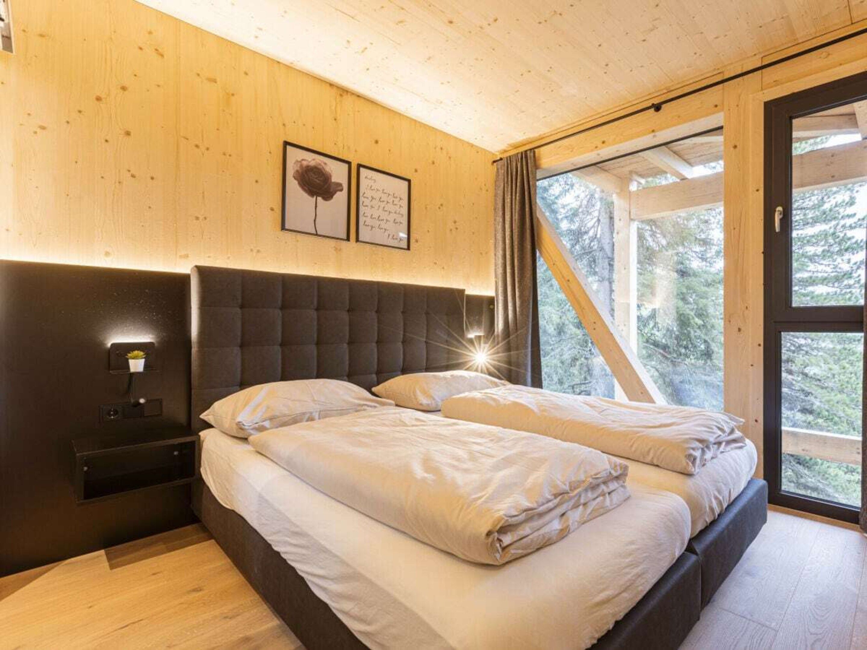 Une chambre avec un grand lit, une table de chevet et une fenêtre donnant sur des arbres.
