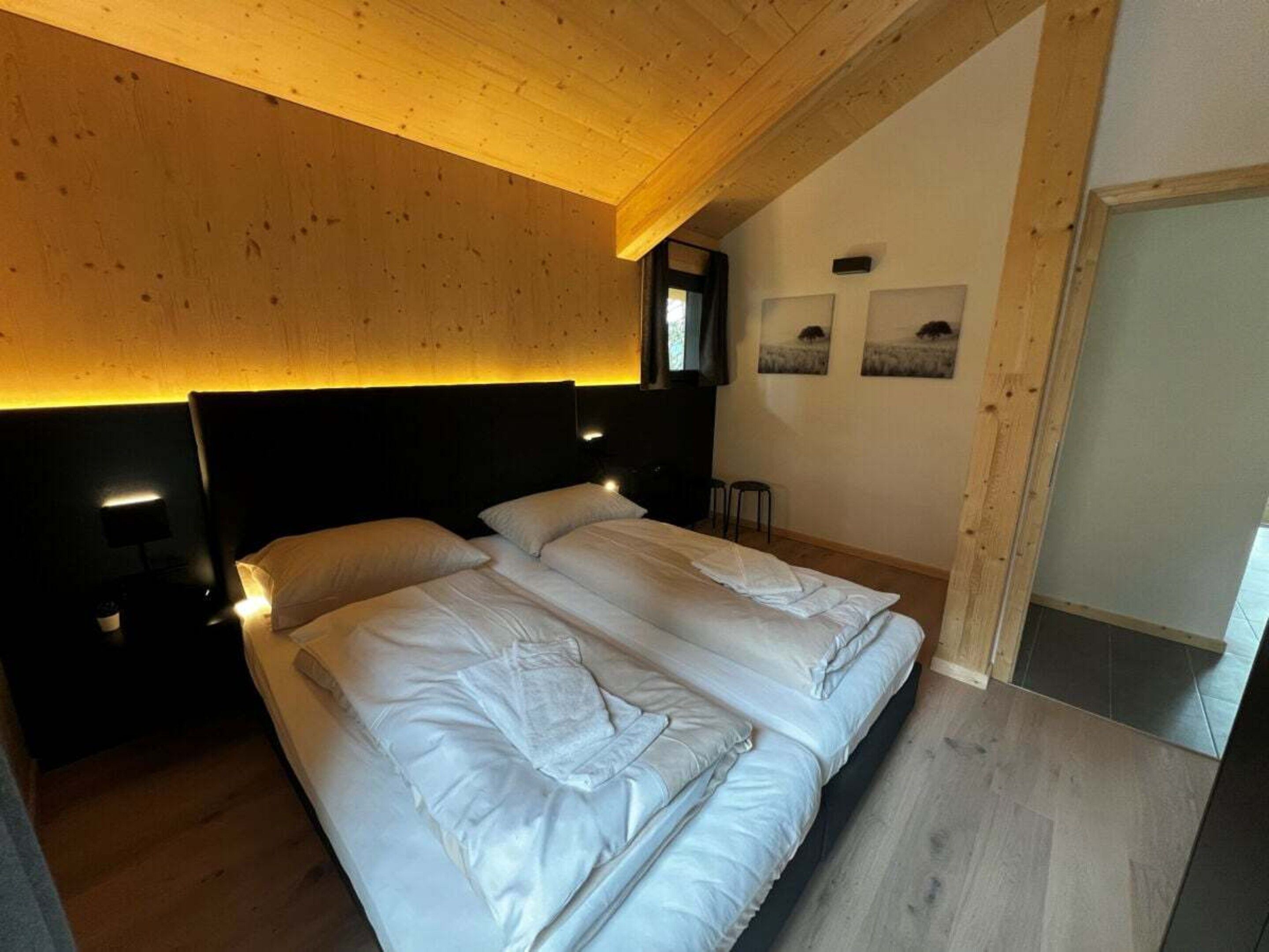 A bedroom with a large bed, wooden ceiling, and wall-mounted lights.