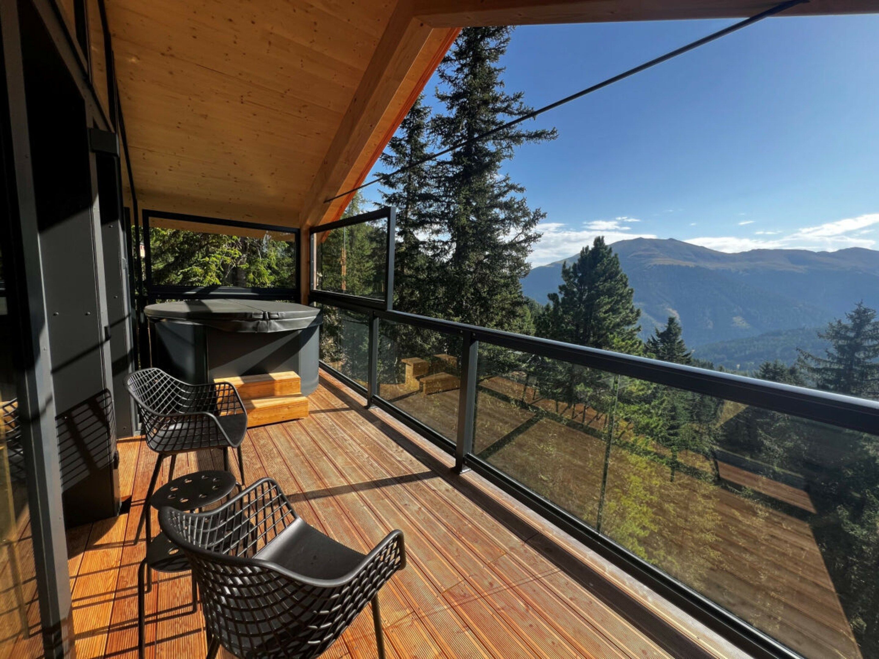 A balcony with a wooden floor, two black chairs, and a table.