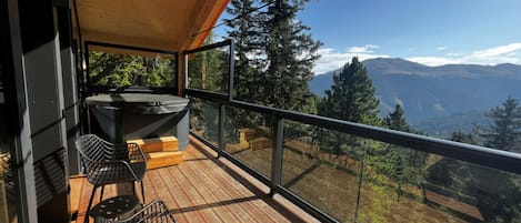 Un balcon avec un plancher en bois, deux chaises noires et une table.