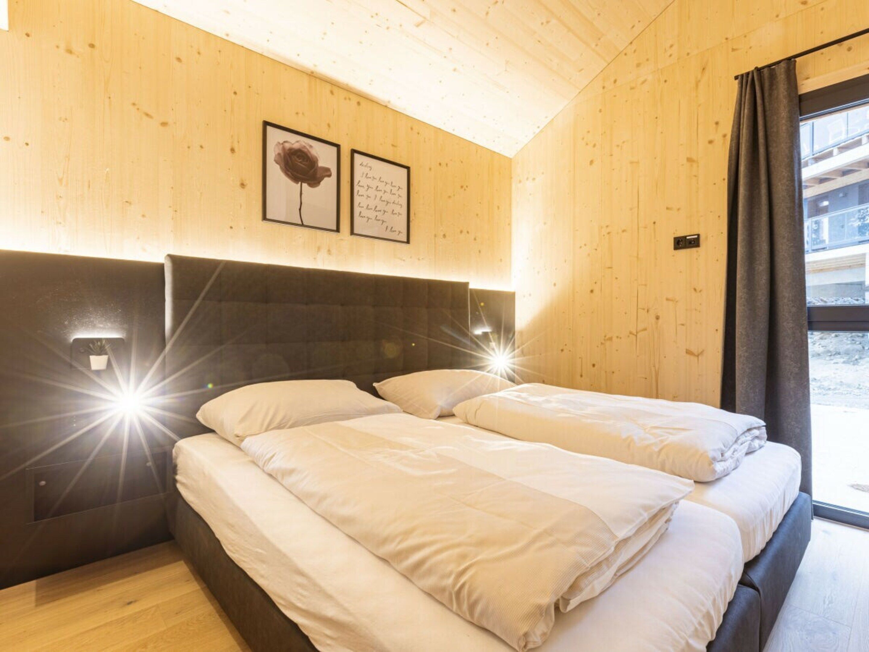 A wooden interior with a bed, a headboard, and a window with curtains.