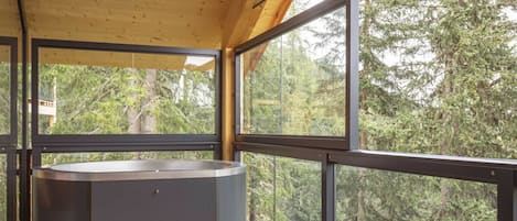 A modern interior with a large window, a wooden deck, and a hot tub.