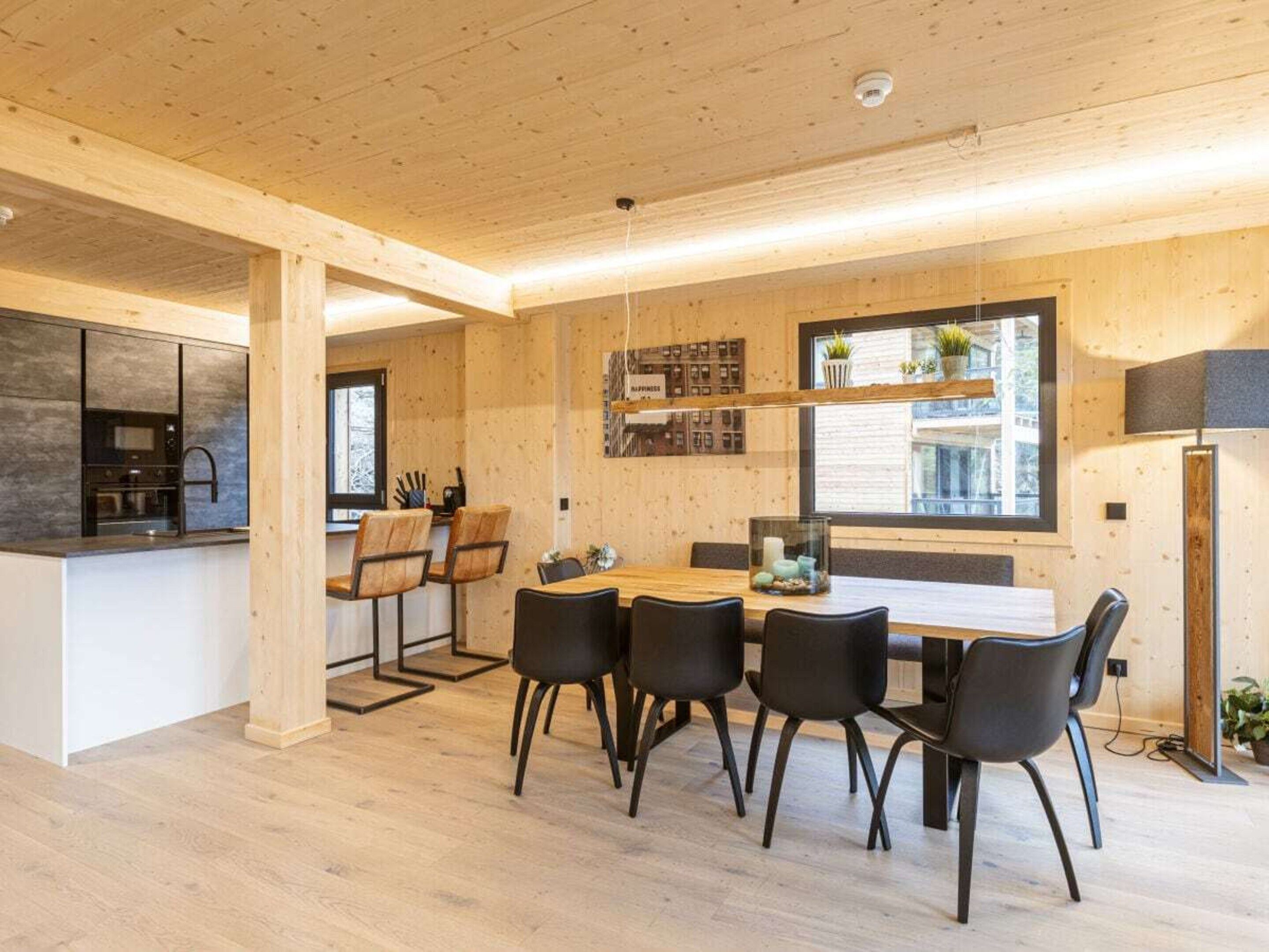 Une cuisine moderne dotée d’un four et d’un micro-ondes encastrés, un coin repas avec une table et des chaises en bois, et une grande fenêtre laissant entrer la lumière naturelle.