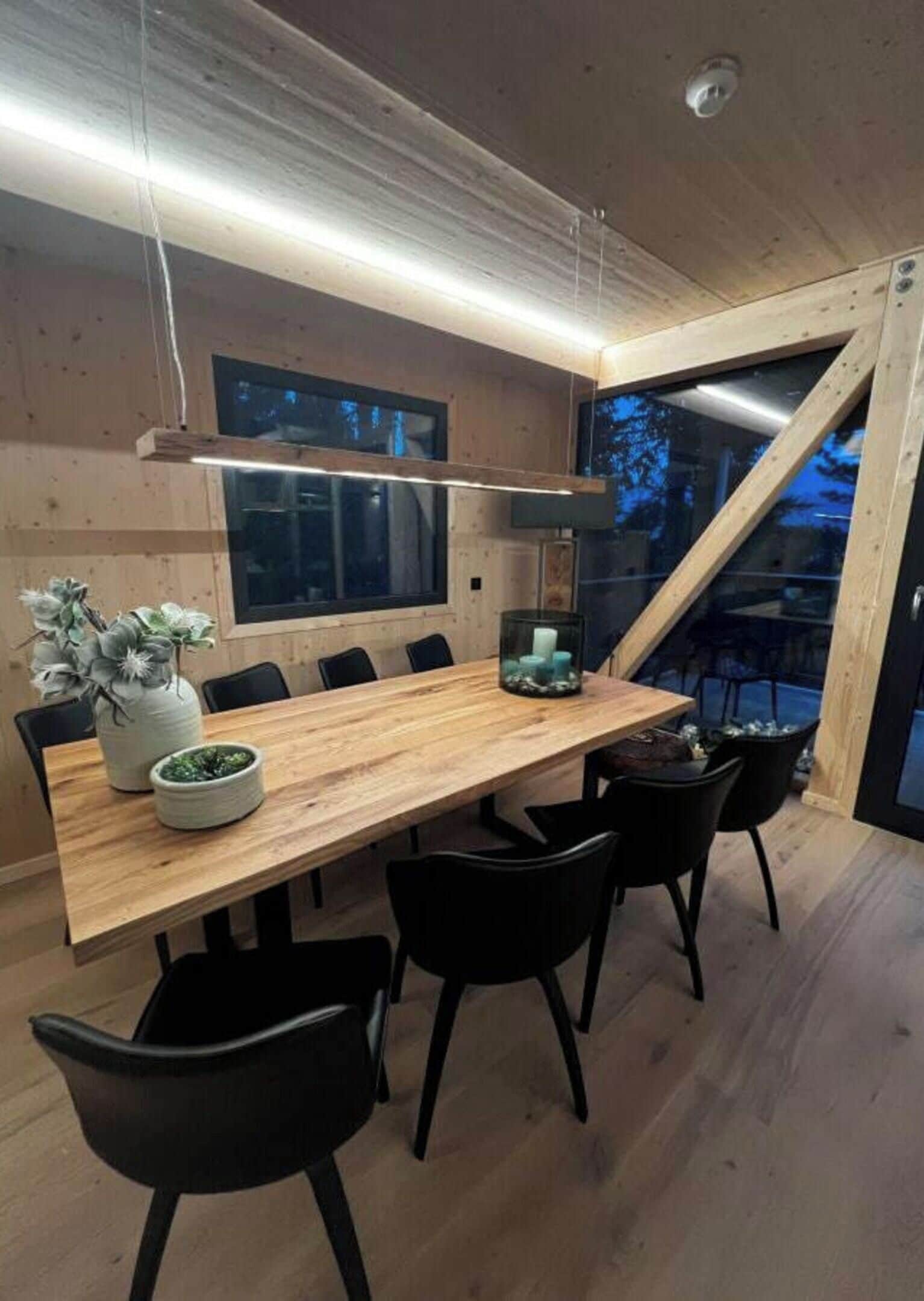 Un espace repas moderne avec une table en bois, des chaises noires et une grande fenêtre.