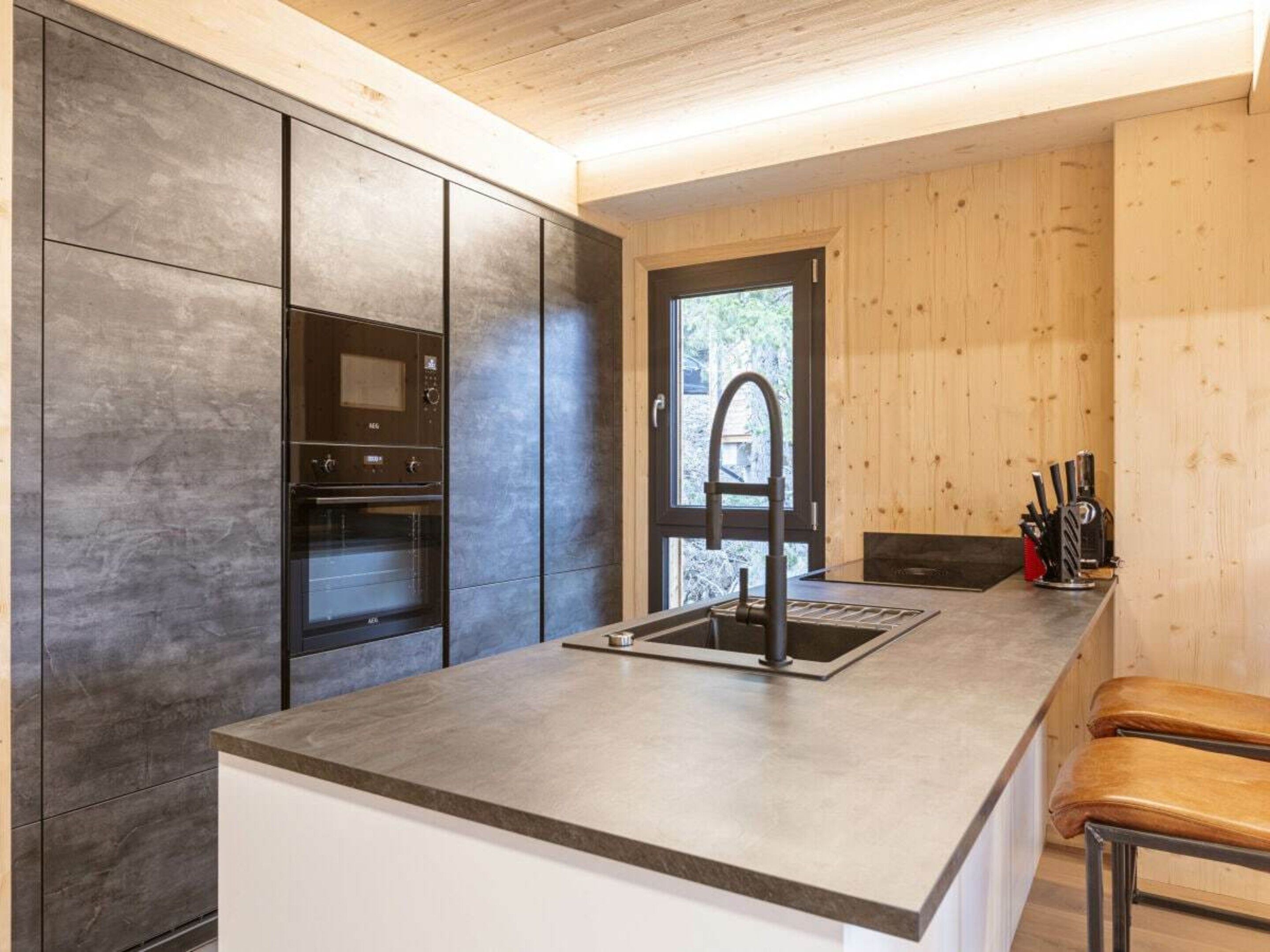 Een moderne keuken met een ingebouwde oven, een RVS spoelbak en houten lambrisering.