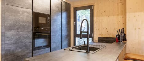 Une cuisine moderne dotée d’un four encastré, d’un évier en acier inoxydable et de panneaux muraux en bois.