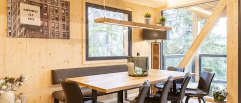 A modern dining area with a wooden table, black chairs, and a large window offering a view of trees.