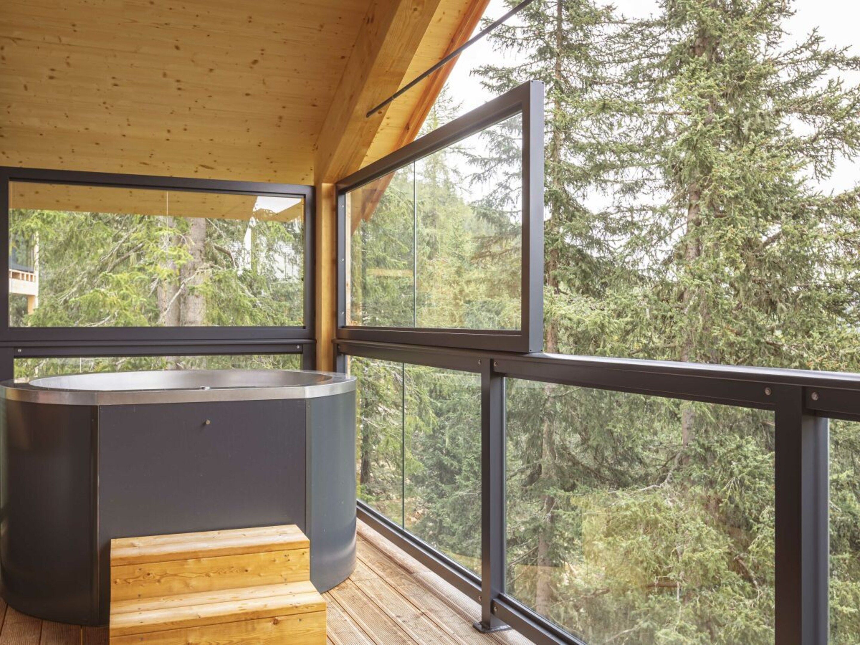 Un interior moderno con un ventanal grande, una terraza de madera y un jacuzzi integrado.