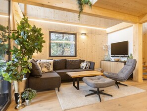 A modern living room with a wooden ceiling, a sofa, a coffee table, a grey armchair, and a TV. - Superior Chalet #14 With Sauna & Hot Tub (Stadl-Predlitz)
