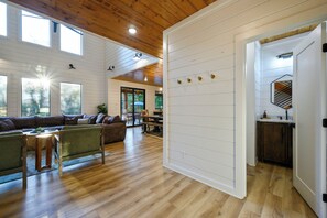 A spacious living area with a wooden ceiling, large windows, a leather sofa, and a dining area. - Resort Pool & Hot Tub | Arcade + Bunk Room (Broken Bow)