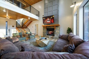A spacious living room with a stone fireplace, a large TV mounted above it, and a comfortable seating area with leather sofas. - Resort Pool & Hot Tub | Arcade + Bunk Room (Broken Bow)