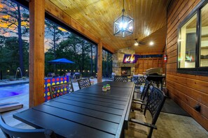 A covered outdoor dining area with a long table, chairs, and a fire feature. - Resort Pool & Hot Tub | Arcade + Bunk Room (Broken Bow)