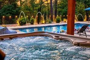 A hot tub with a pool in the background, surrounded by lounge chairs and string lights. - Resort Pool & Hot Tub | Arcade + Bunk Room (Broken Bow)