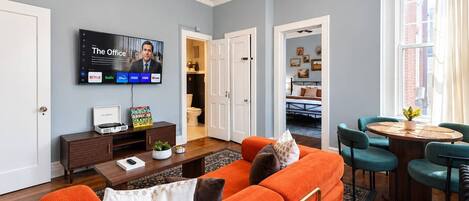 Una sala de estar con sofá, mesa de centro y televisor montado en la pared.