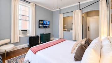 Ein Schlafzimmer mit einem Bett, einem Fernseher, einem Heizkörper, einem Stuhl und einem Fenster mit Vorhängen.