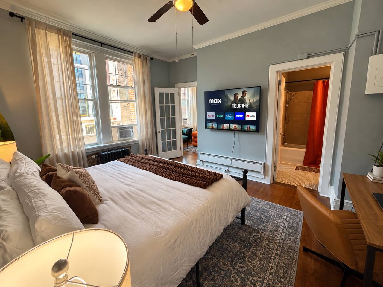 A modern hotel room with a large bed, a flat-screen TV, a shower area, and a dining table.