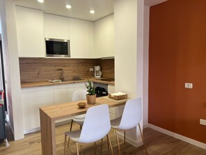 A compact kitchen with white cabinets, a wooden countertop, a microwave, a coffee maker, and a dining area with two white chairs. - Andorra 5 - Studio with pool view (Playa de las Américas)