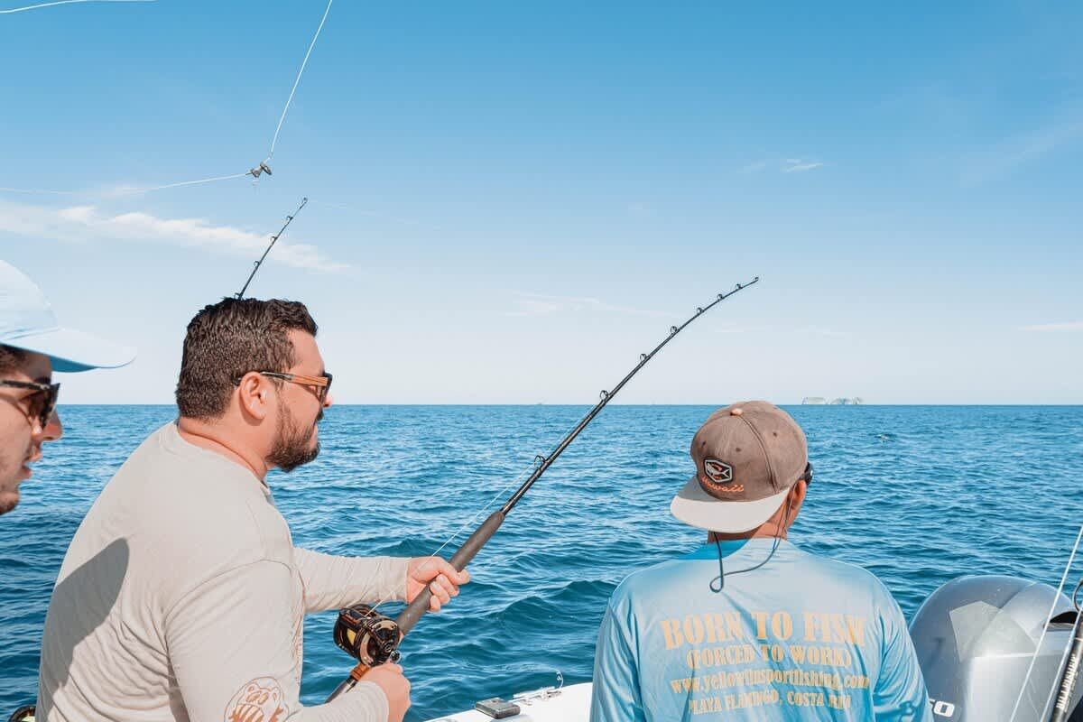 Un bote con dos personas pescando, una lleva gorra y camiseta con texto, y la otra sostiene una caña de pescar.