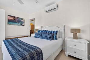 Un dormitorio con cama, mesitas de noche, un equipo de aire acondicionado y un cuadro en la pared.