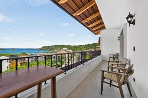 Ein Balkon mit Holztisch und -stühlen, einem Geländer und Blick auf das Meer und die Gebäude.