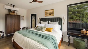 A bedroom with a bed, a ceiling fan, a window with a view, a dresser, and a bedside table. - Romantic Escape with Private Heated Pool & Sauna (Fife Lake)