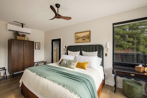 A bedroom with a bed, a ceiling fan, a window with a view, a dresser, and a bedside table. - Romantic Escape with Private Heated Pool & Sauna (Fife Lake)