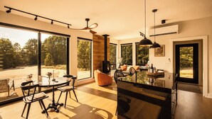 A spacious living area with a dining table, chairs, and a large window offering a view of the outdoors. - Romantic Escape with Private Heated Pool & Sauna (Fife Lake)