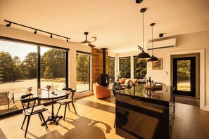 A spacious living area with a dining table, chairs, and a large window offering a view of the outdoors. - Romantic Escape with Private Heated Pool & Sauna (Fife Lake)