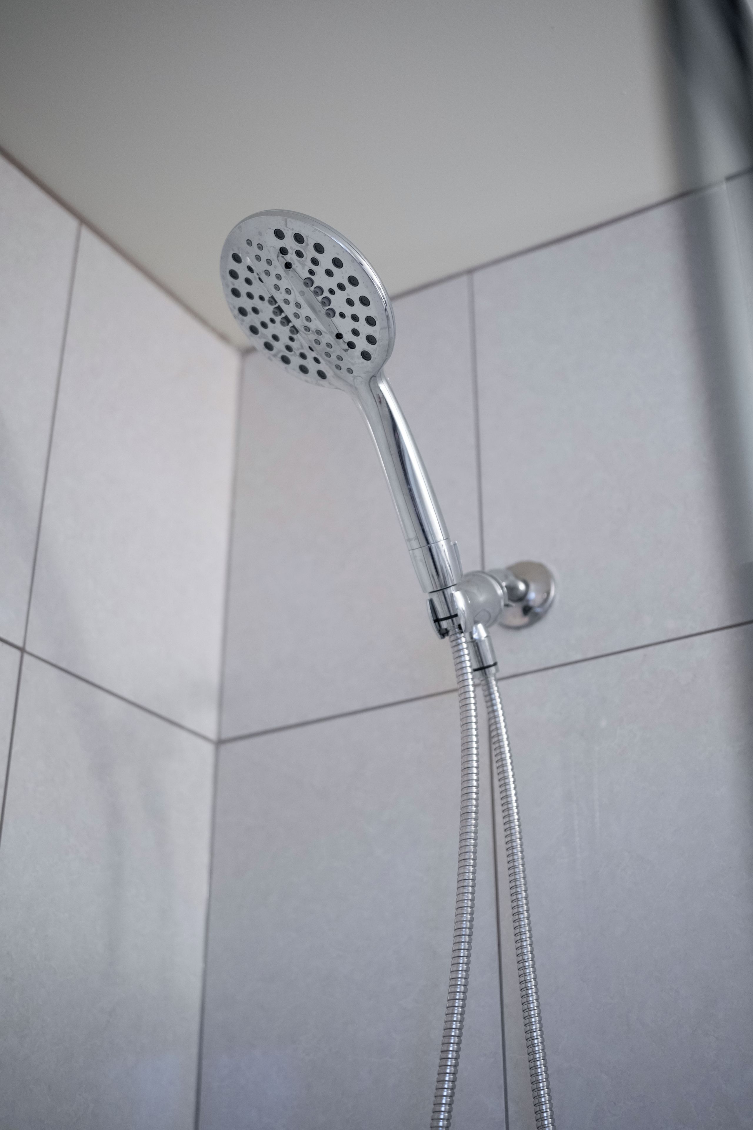 Ein Duschkopf mit flexiblem Schlauch, an einer gefliesten Wand befestigt.