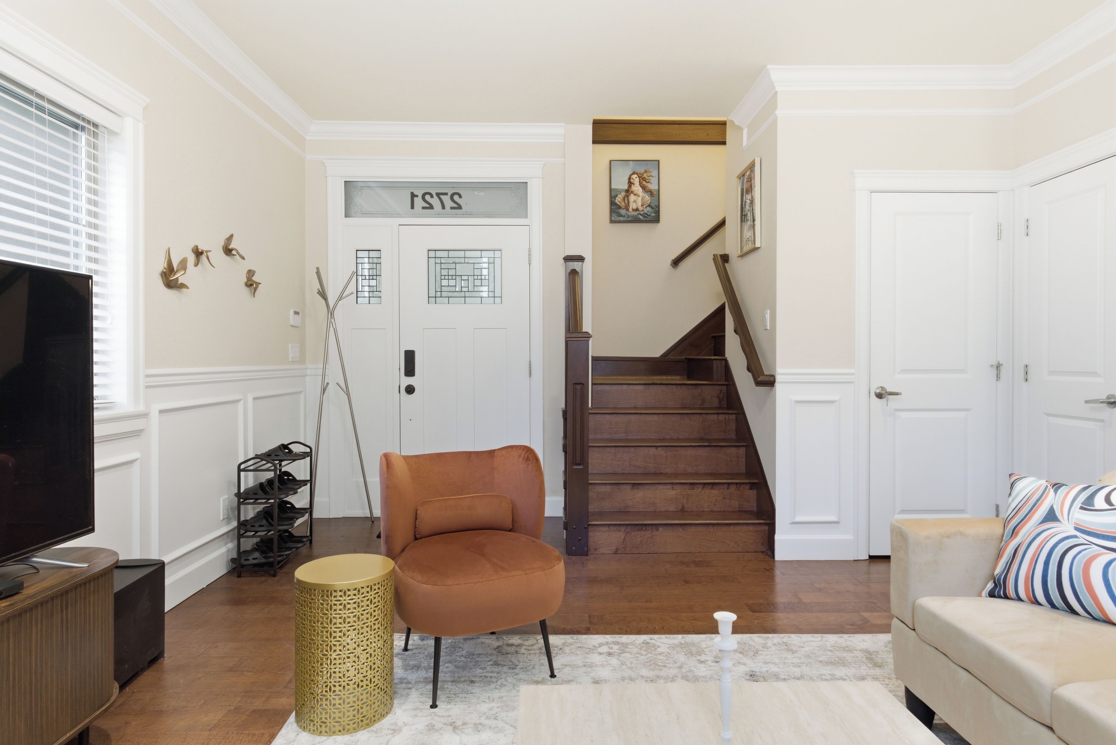 A living room with a television, a sofa, a chair, a staircase, and a door with a sign.