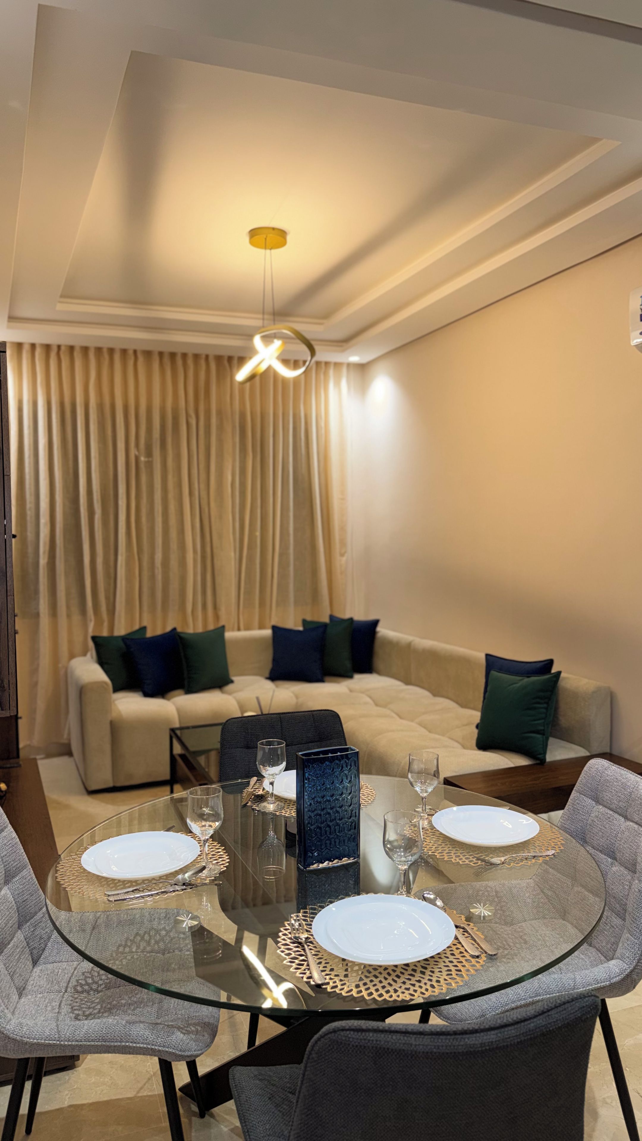 A dining area with a glass table, chairs, and a sofa with cushions.