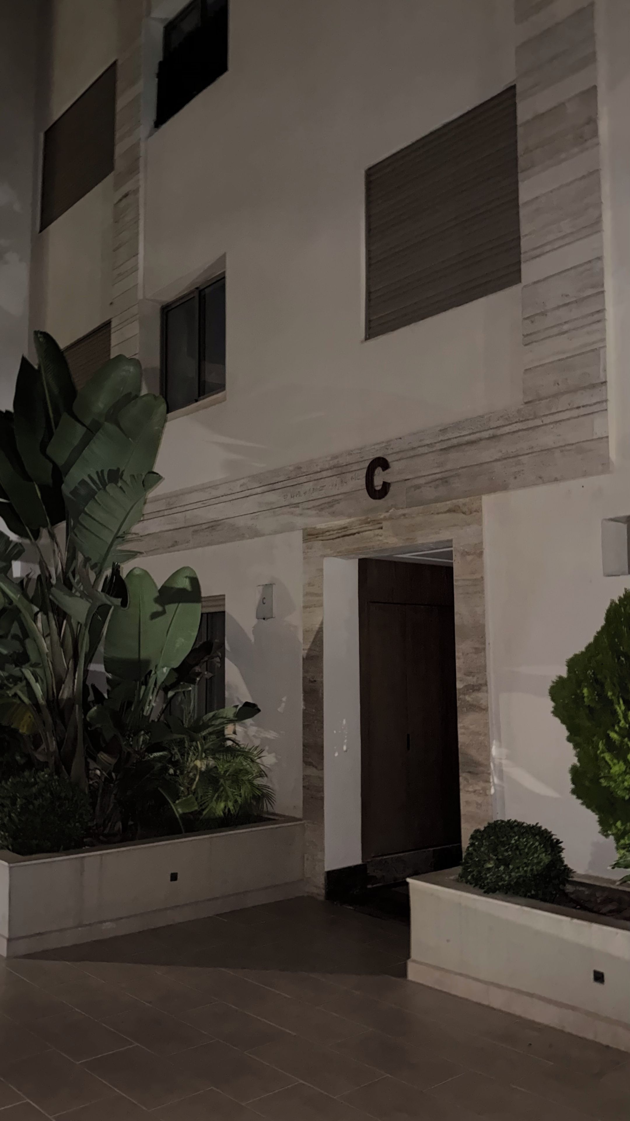 Un bâtiment avec un panneau en forme de « C », une porte et des plantes en pot.