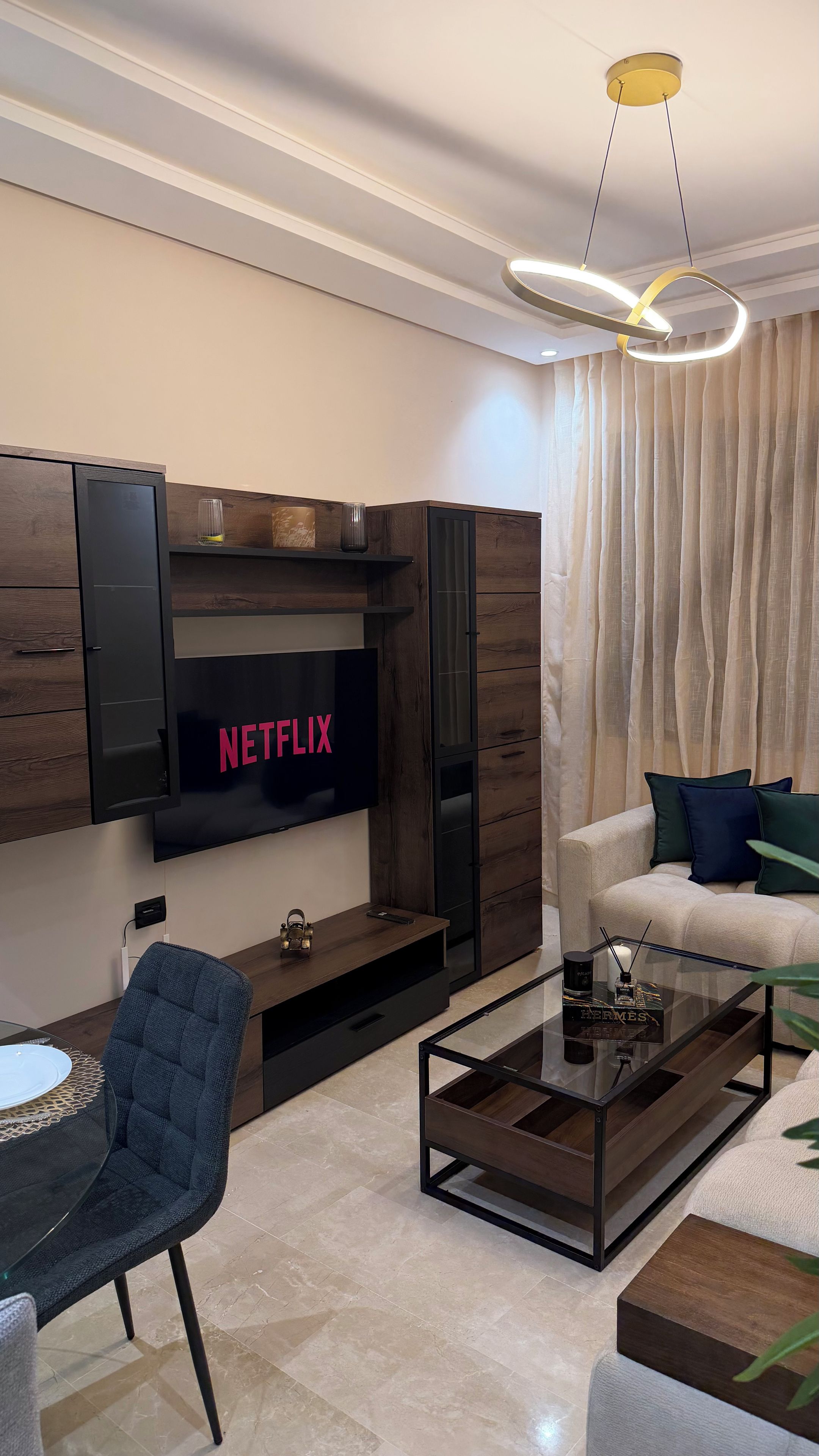 Een moderne woonkamer met een flatscreen televisie aan de muur, een salontafel, een bank en een fauteuil.