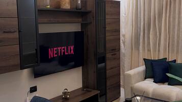 Een moderne woonkamer met een flatscreen televisie aan de muur, een salontafel, een bank en een fauteuil.