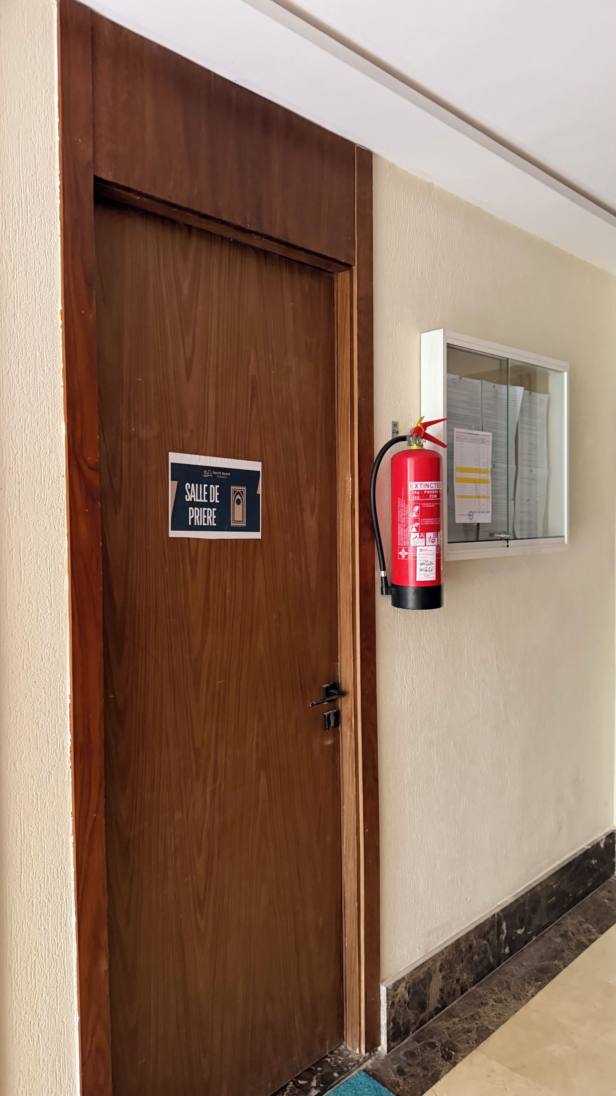 A wooden door with a sign indicating a room for the disabled, a fire extinguisher mounted on the wall, and a window with papers.