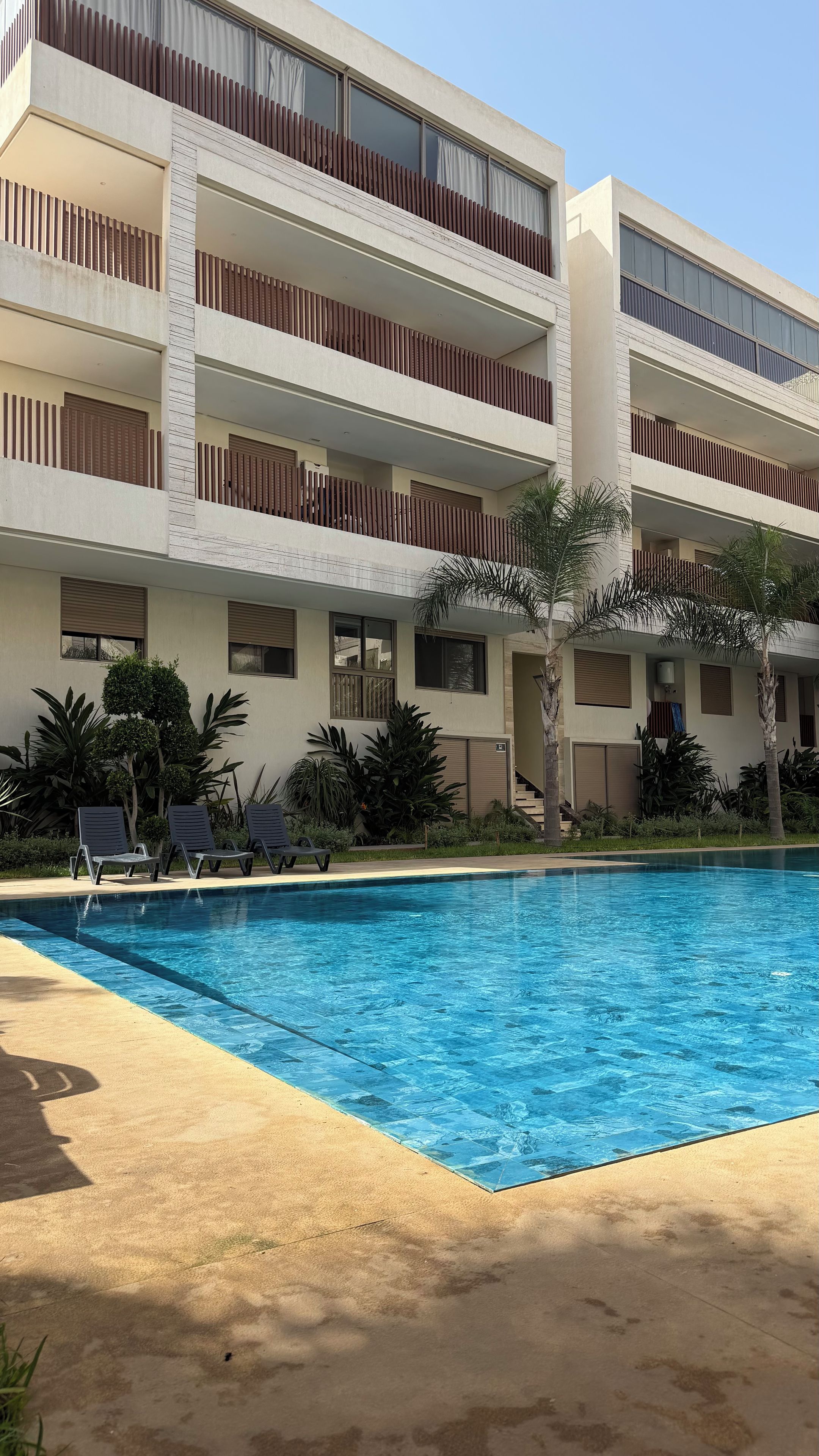 A multi-story hotel with a swimming pool, outdoor seating, and tropical landscaping.